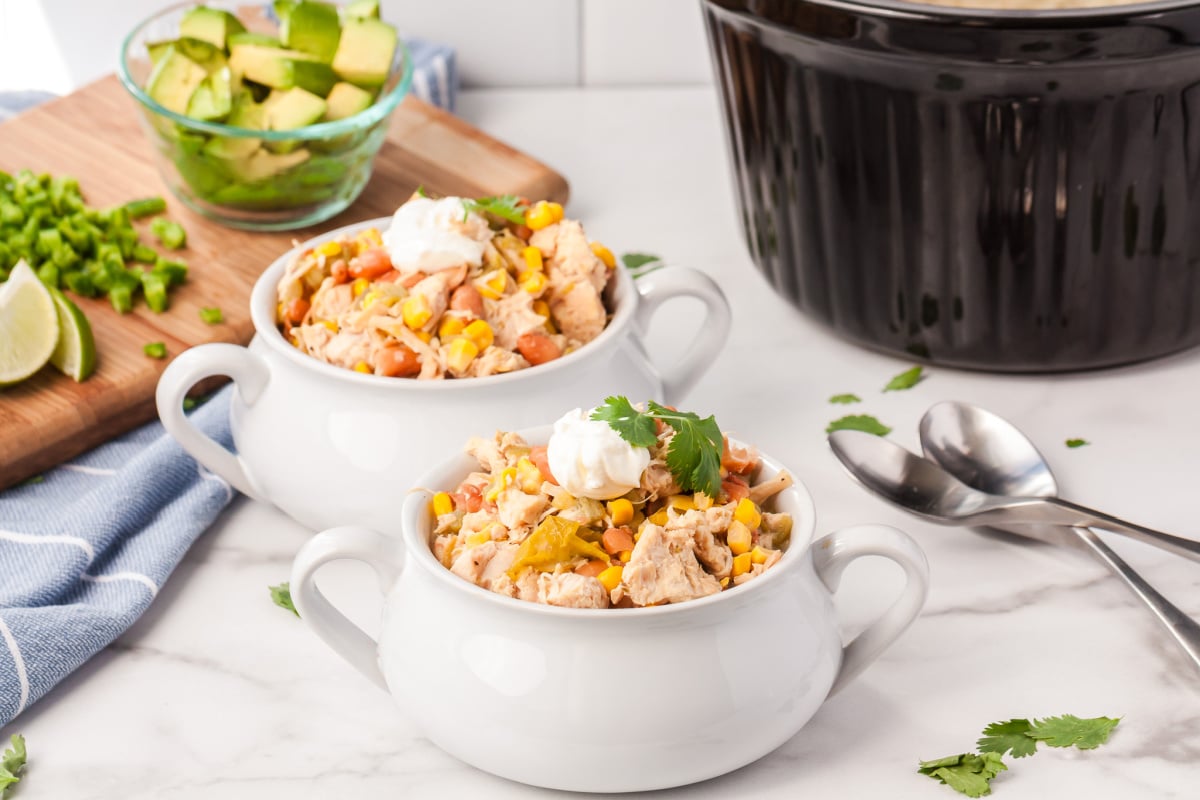 two bowls of chili with a bowl of avocados and a crockpot of chili in the background