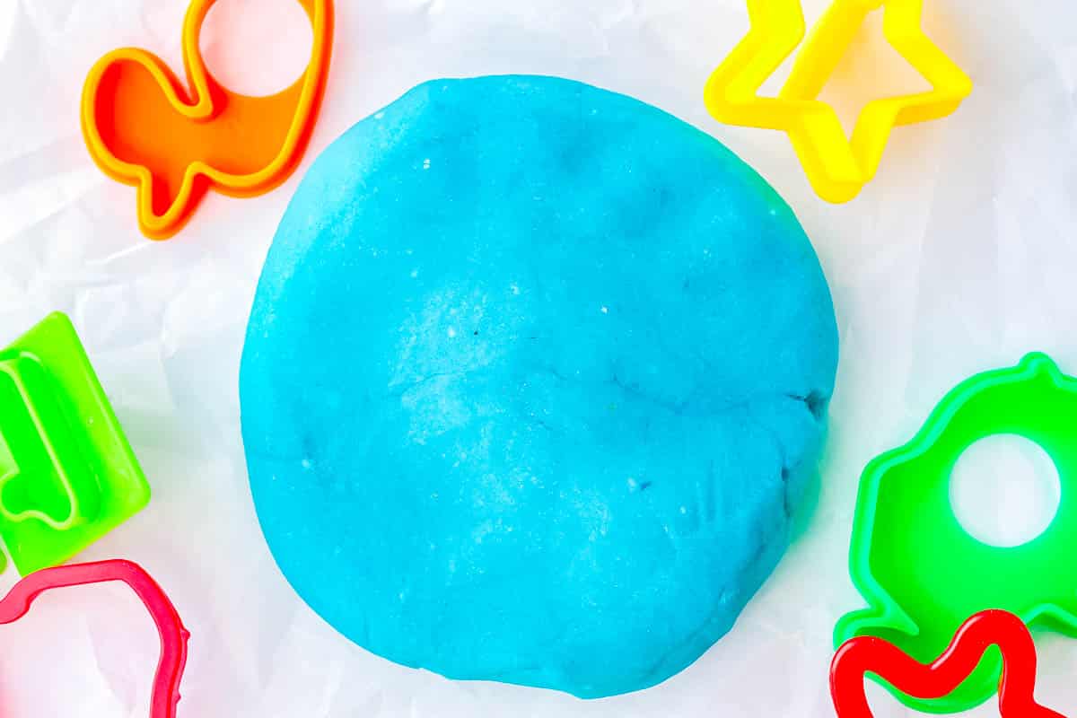 A blue mound of homemade playdough on a work surface with cookie cutters around it.