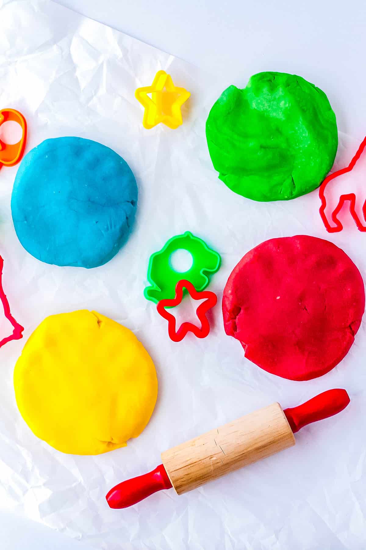Blue, green, yellow, and red playdough with cookie cutter and a small rolling pin nearby.