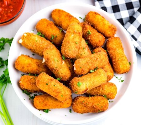 Fried Mozzarella Cheese Sticks on a white plate with dipping sauce in the background.
