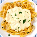 A square picture of the finished fettuccine alfredo on a white plate with chopped fresh parsley.