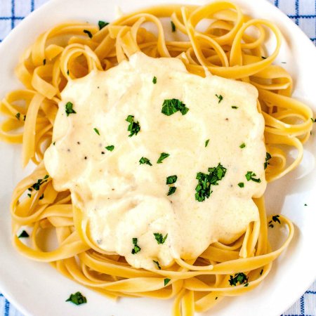 A square picture of the finished fettuccine alfredo on a white plate with chopped fresh parsley.