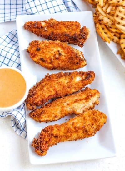 Overhead picture of homemade chicken fingers on a platter with a small bowl of dipping sauce.