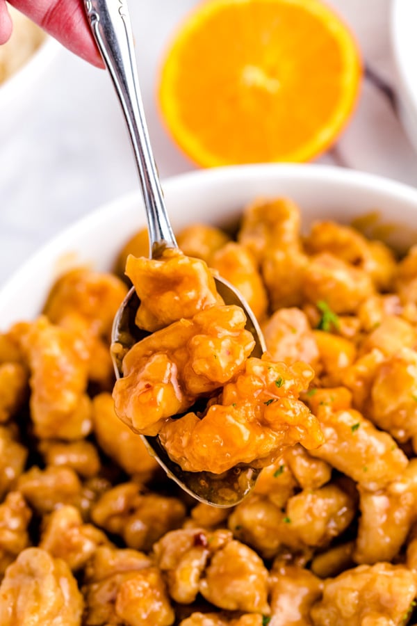A spoon lifting up pieces of Panda Express Orange Chicken. 