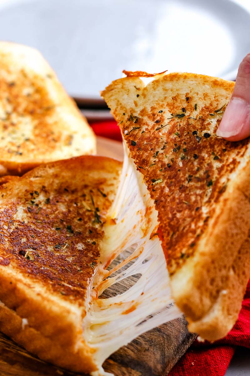 A Pizza Grilled Cheese cut in half and being pulled apart.