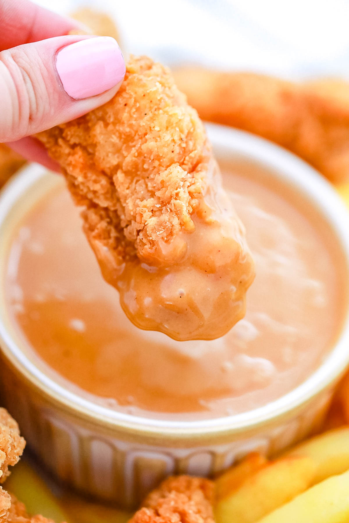 A close up picture of a chicken strip being dipped into the sauce.