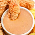 An overhead picture of the finished Copycat Chick-Fil-A Sauce with a chicken strip wing dipped into it.