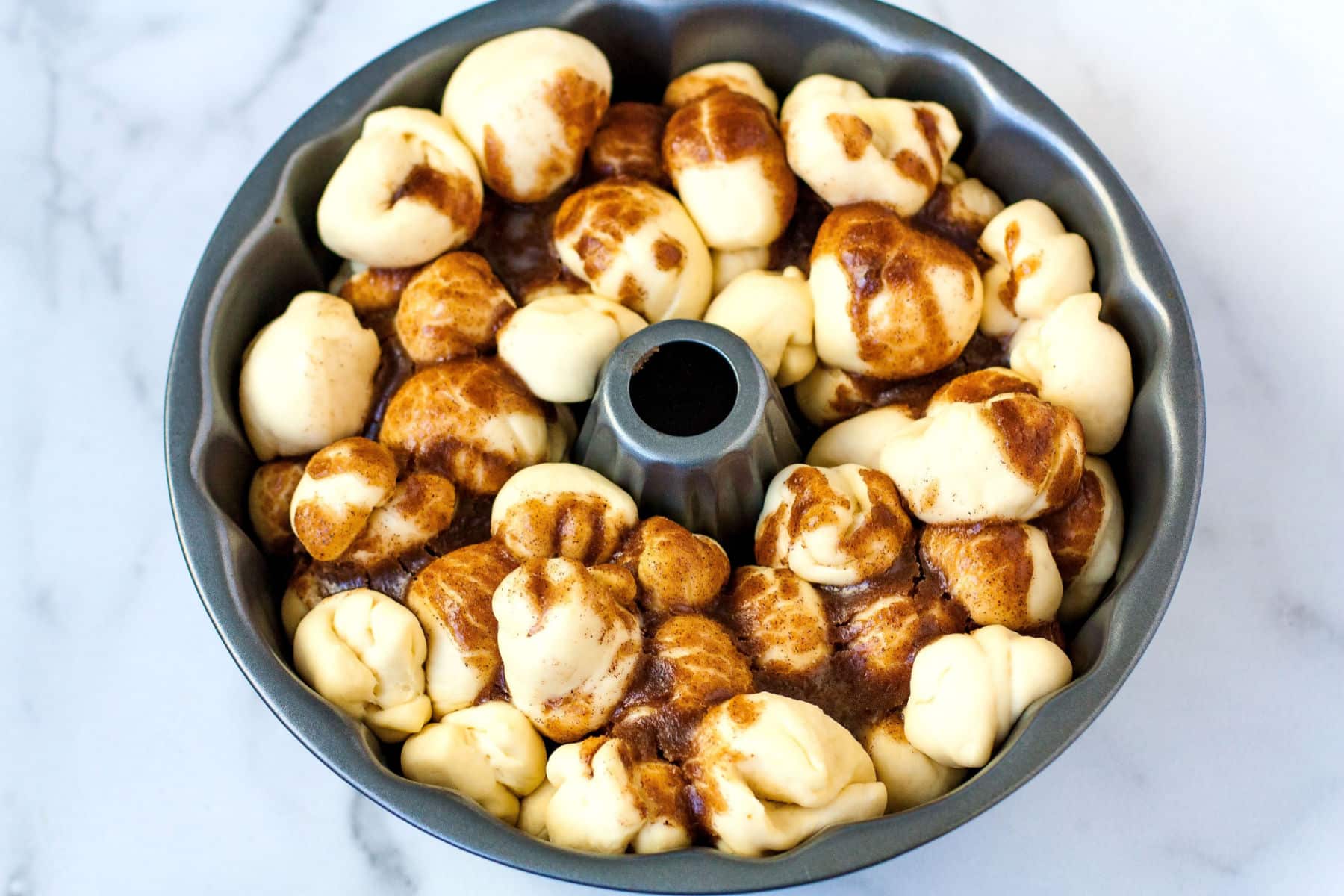 a bundt pan with raw dough balls and butter sugar mixture poured over the dough balls