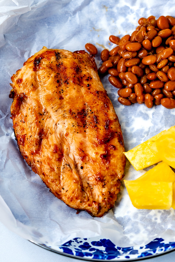 Grilled BBQ Chicken Breast on a blue plate with baked beans and fresh pineapple.