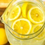 A close up picture of lemonade with slices of lemons in a glass pitcher.