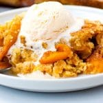 Close up of peach cobbler with a scoop of vanilla ice cream on a white plate.
