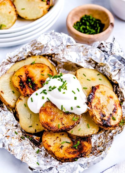 The finished grilled potatoes in foil topped with sour cream and chives.