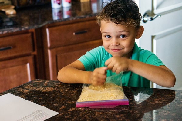 A little boy crushing up crackers in a Ziplock bag.