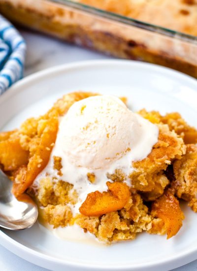 Warm peach cobbler on a white plate with a scoop of vanilla ice cream on top.
