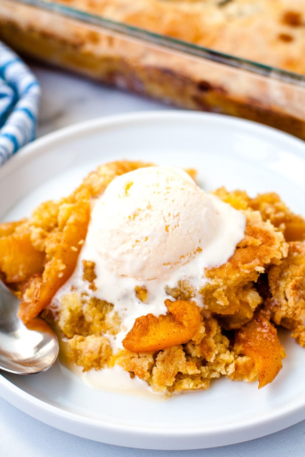 Warm peach cobbler on a white plate with a scoop of vanilla ice cream on top. 