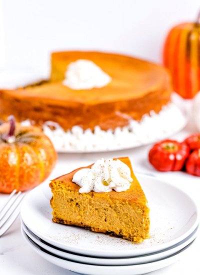 A slice of pumpkin cheesecake on a white plate and garnished with whipped cream.