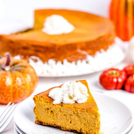 A slice of pumpkin cheesecake on a white plate and garnished with whipped cream.