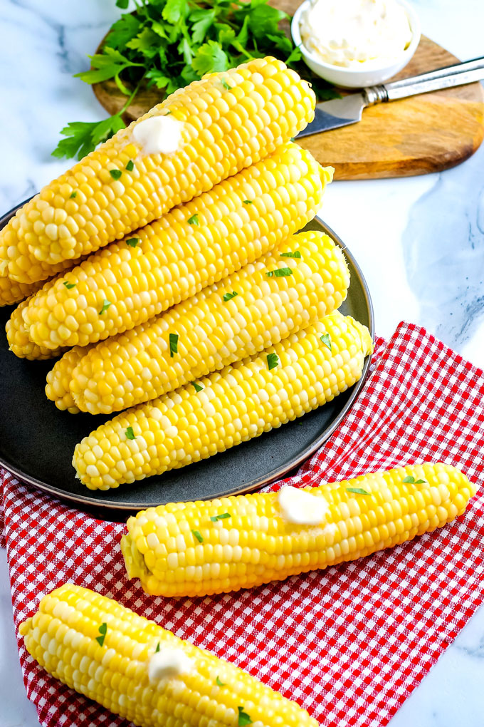 Steamed corn on a platter that's covered with melted butter and chopped parsley.