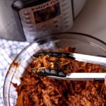 Tongs picking up a scoop of Instant Pot Pulled Pork.