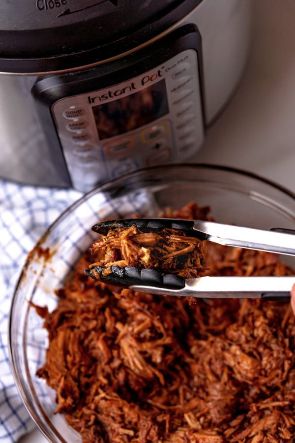 Tongs picking up a scoop of Instant Pot Pulled Pork.