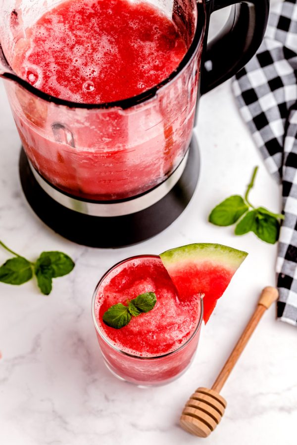 Overhead picture of watermelon smoothie in a clear glass and more in a blender.