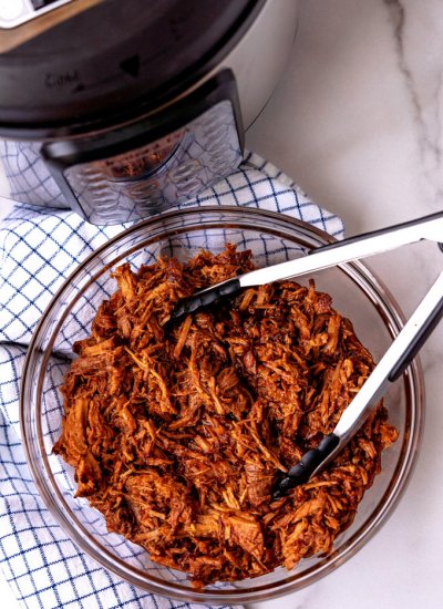 An overhead picture of a bowl full of shredded pork with an Instant Pot in the background.