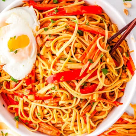 a bowl of thai noodles with a fried egg on top and chopsticks in the bowl
