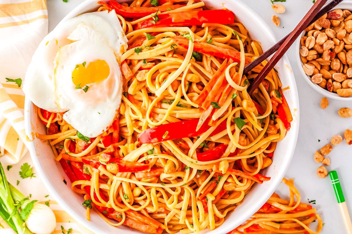 a bowl of thai noodles with a fried egg on top and chopsticks in the bowl