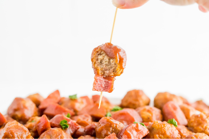 A toothpick lifting up a cranberry meatball with smoked sausage.