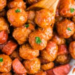 A wooden spoon lifting up cranberry meatballs from the slow cooker.