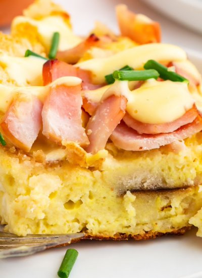 A slice of overnight eggs benedict casserole on a white plate with hollandaise sauce drizzled over it.