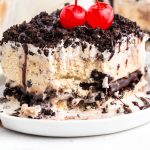 A slice of Oreo ice cream cake on a white plate topped with cherries.