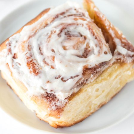 A close up picture of an overnight cinnamon roll on a white plate.