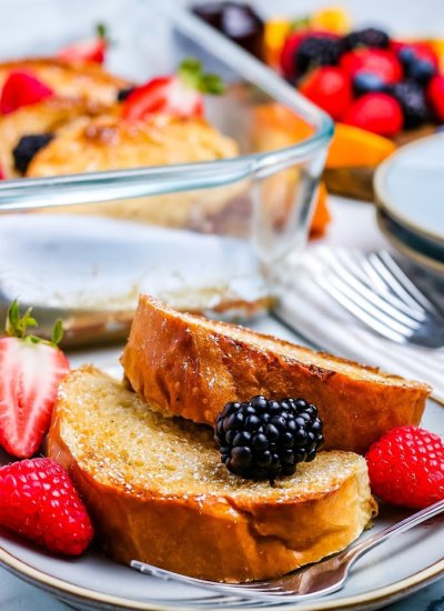 Two slices of overnight French toast bake on a plate with berries.