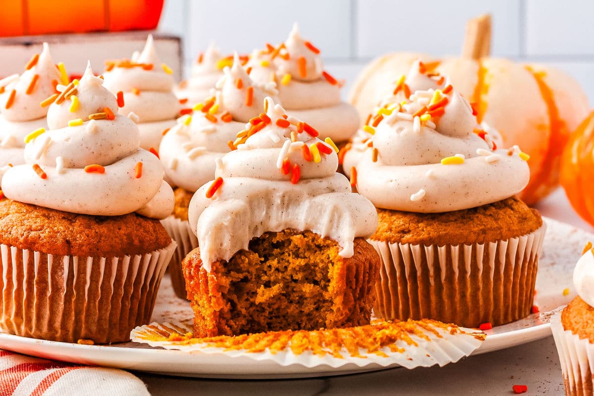 Freshly baked pumpkin cupcakes topped with creamy cinnamon cream cheese frosting with a bite taken out of one of the cupcakes