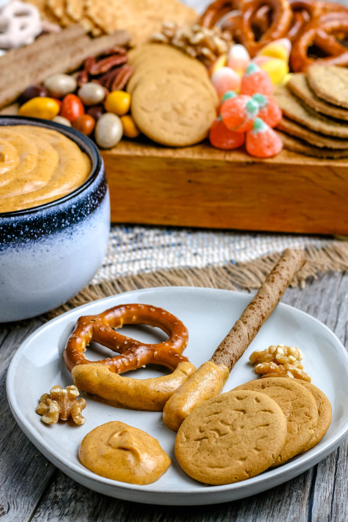 pretzels, cookies, and nuts on a white plate with some dip on the plate, too.