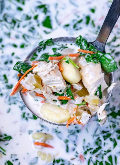 A close up picture of slow cooker chicken gnocchi soup in a soup ladle.