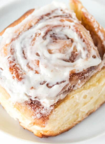 A close up picture of an overnight cinnamon roll on a white plate.