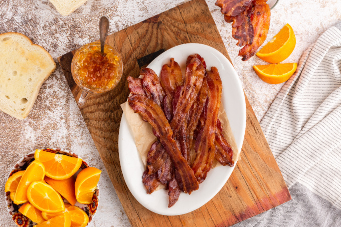 An overhead picture of candied bacon on a white serving platter with sliced oranges around it.
