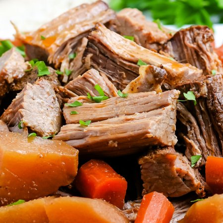 Shredded pot roast on a white platter with roasted potatoes and carrots.