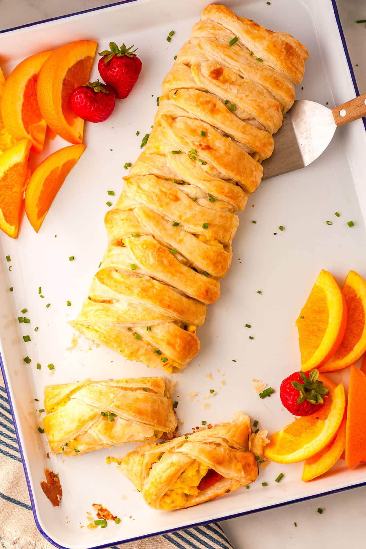 eggs benedict braid on a baking sheet with fruit slices