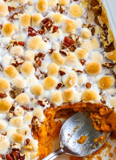 A spoon inside the sweet potato casserole with marshmallows and pecans.