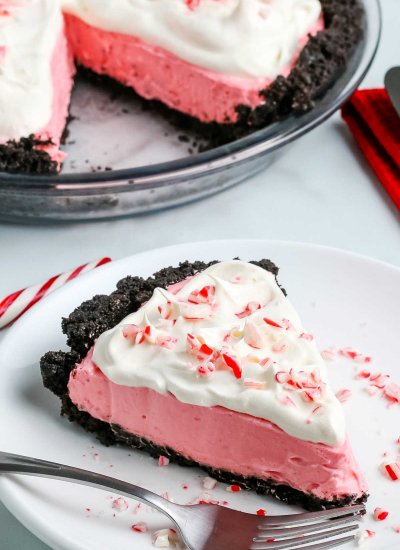 A slice of candy cane pie on a white plate with the entire pie in the background.
