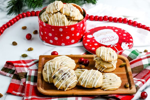 Pistachio cookies on a wooden tray with a tin of cookies for gifting in the background. 