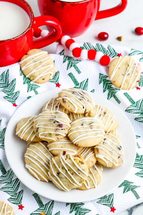 Pistachio Cookies on a white plate with mugs of milk in the background.