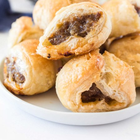 Sausage rolls on a pile on a white plate.