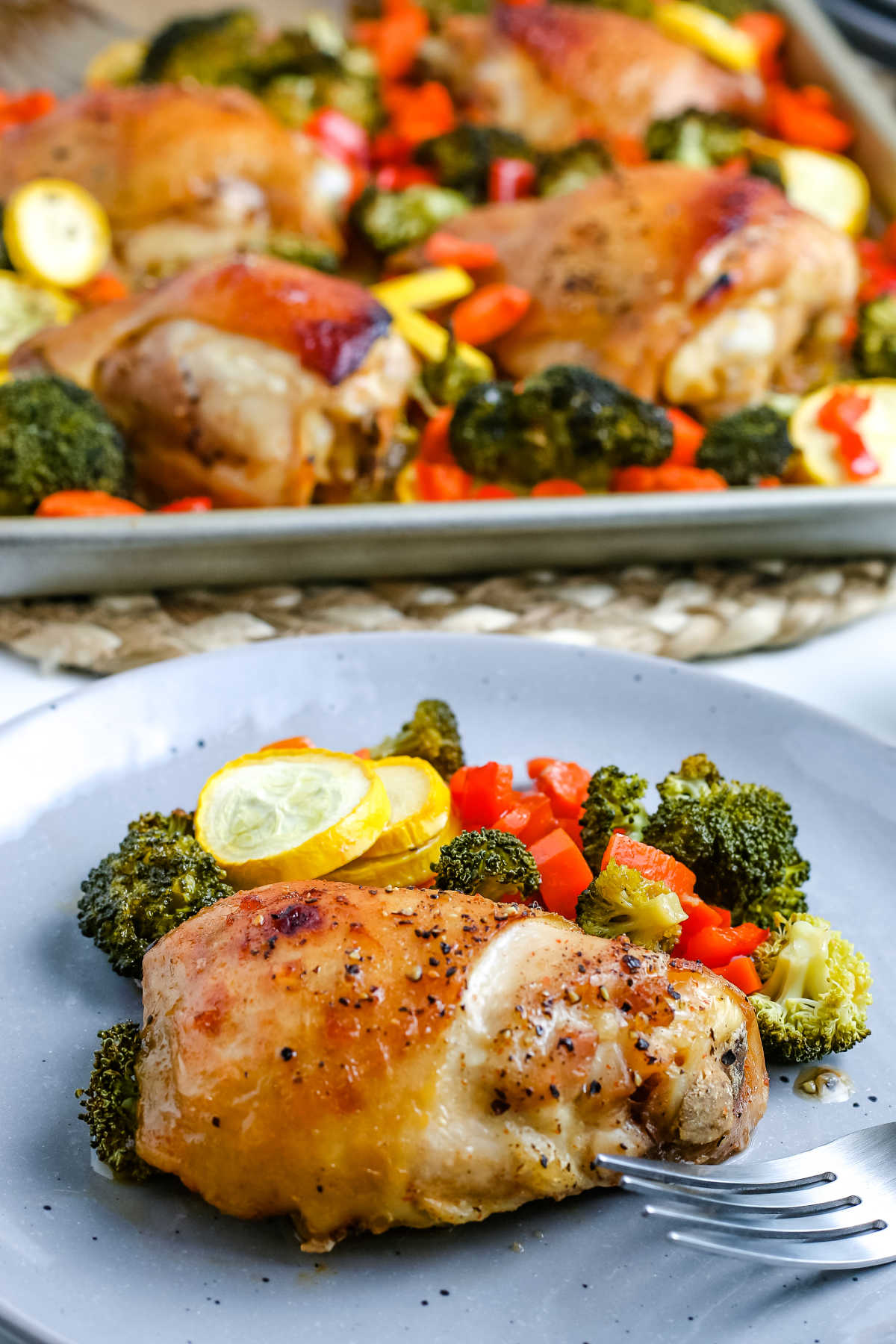 A chicken thigh and vegetables on a grey plate.