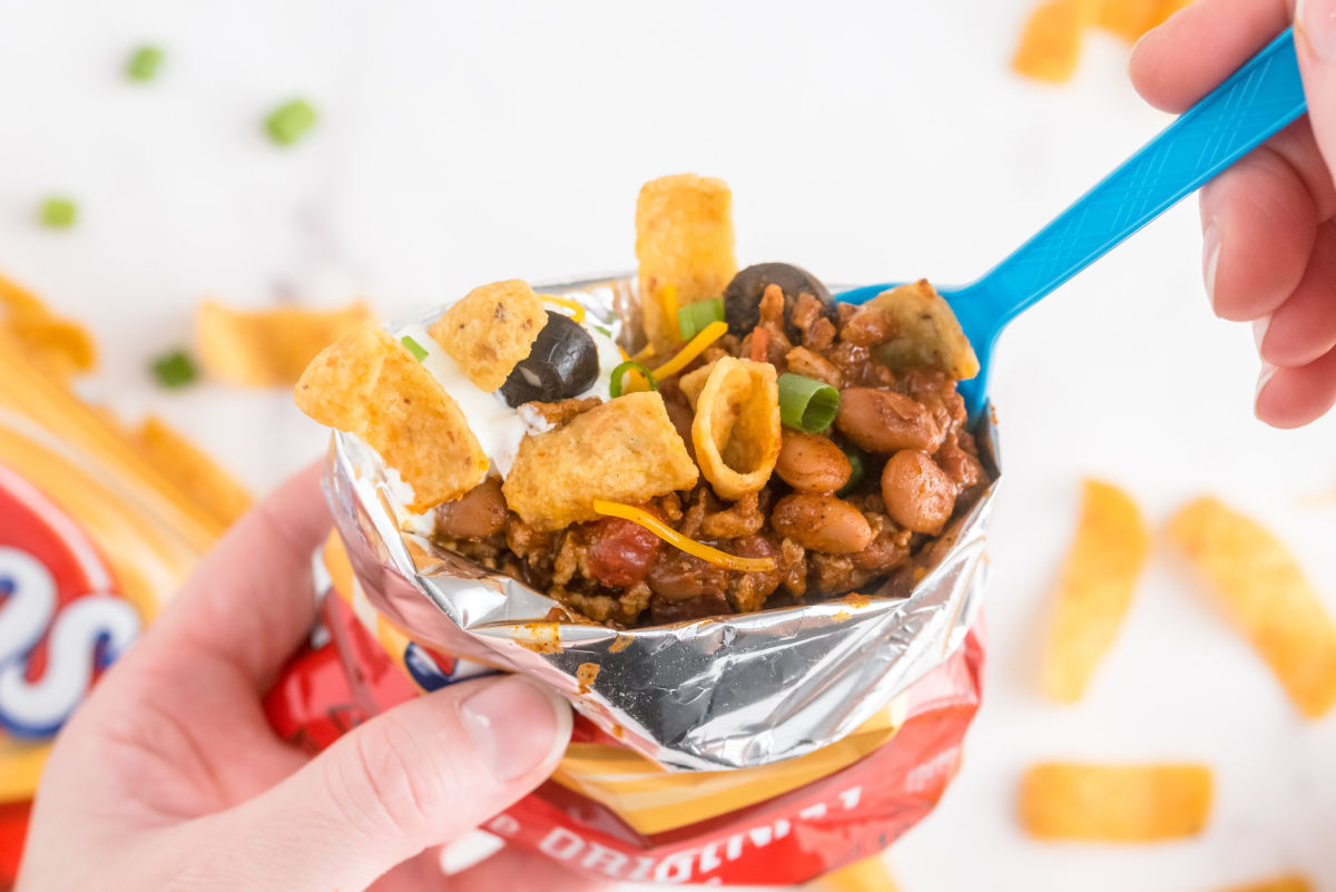 A hand holding a walking taco and a spoon digging into it.