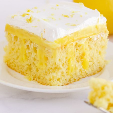 Piece of lemon cake on a plate. A fork is beside it with a piece of cake on it.