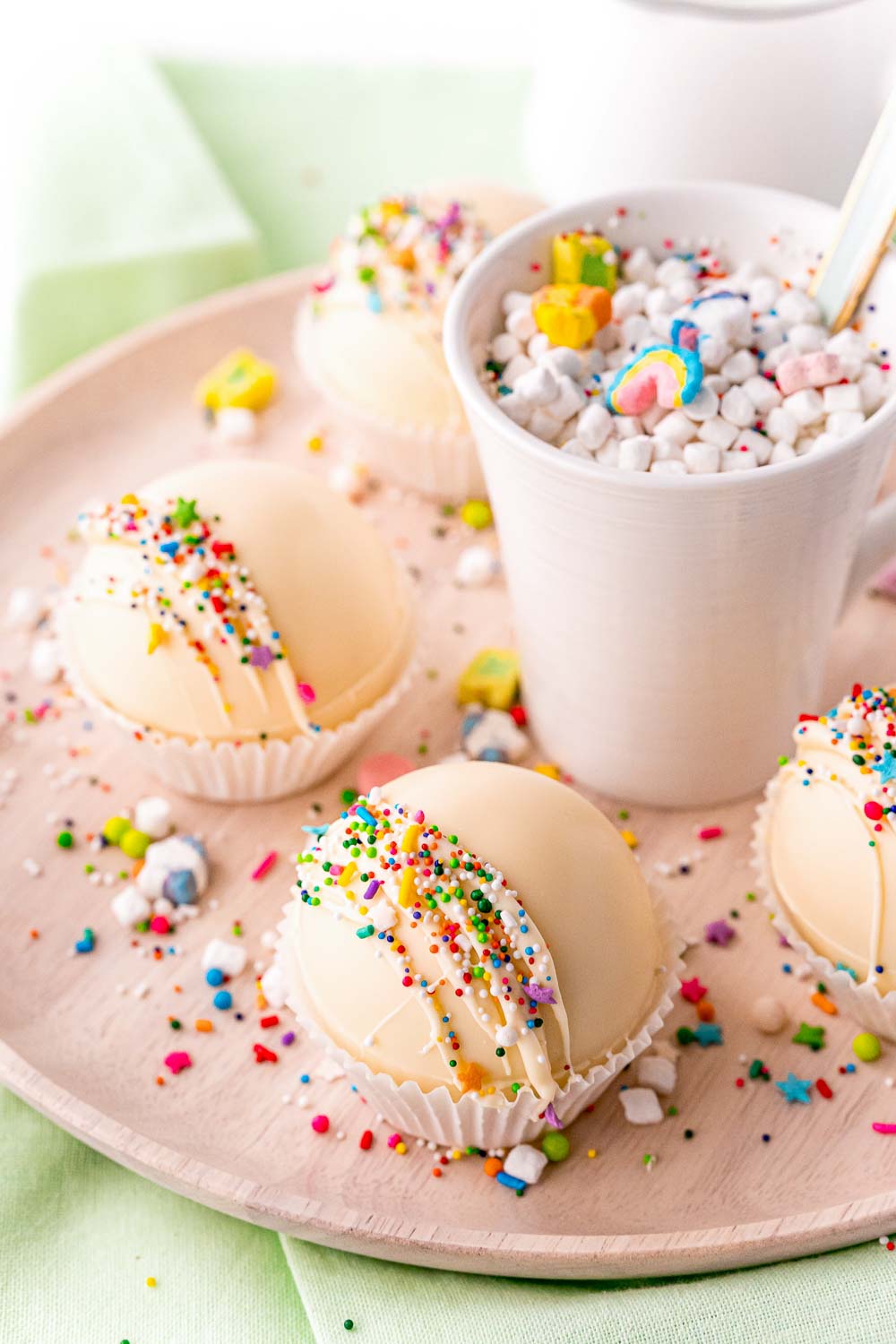 Rainbow White Hot Chocolate Bombs on a platter and in a mug. 